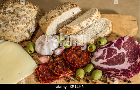 Village rustique, petit déjeuner avec des saucisses, jambon, olives, poivre noir, l'ail, du fromage et du pain fait maison. Banque D'Images