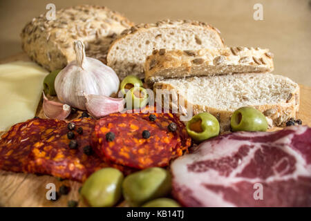 Village rustique, petit déjeuner avec des saucisses, jambon, olives, poivre noir, l'ail, du fromage et du pain fait maison. Banque D'Images