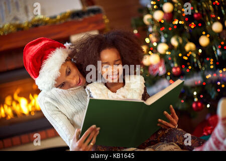 Jolie Jeune femme lisant un livre à sa fille près de l'arbre de Noël, Joyeux Noël Banque D'Images