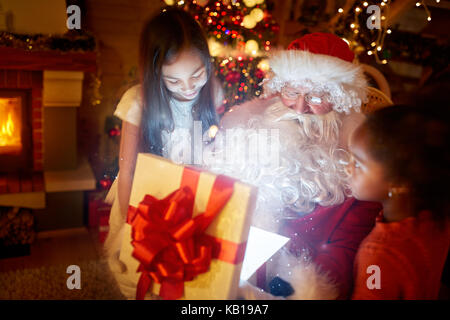 Père Noël cadeau magique d'ouverture tandis que deux filles regardant stupéfait Banque D'Images