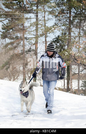 Yung man walking son chien husky dans la forêt enneigée Banque D'Images