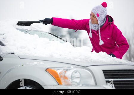 Femme enlever la neige du pare-brise de sa voiture Banque D'Images