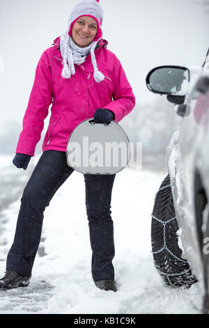 Smiling woman standing next sa voiture avec les chaînes à neige sur le pneu Banque D'Images