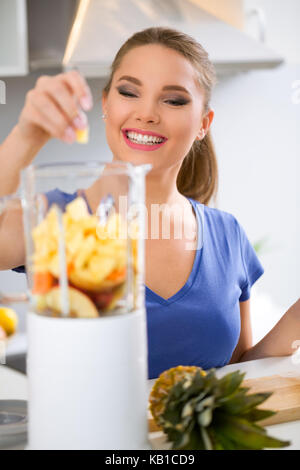 Jeune femme la préparation de boisson avec de l'ananas, fruits des smoothies avec blender Banque D'Images