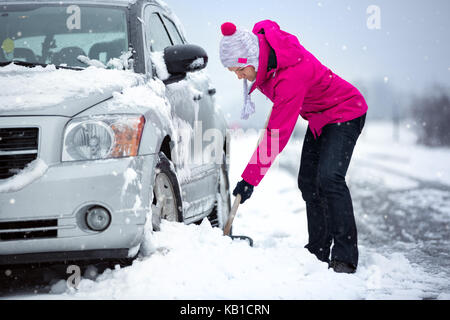 Femme pelletant et enlever la neige de sa voiture, coincé dans la neige Banque D'Images