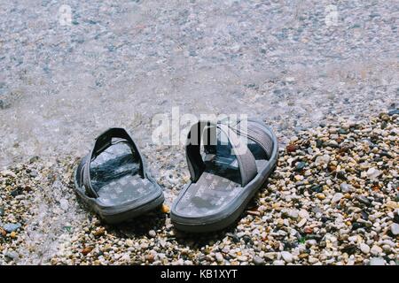 Men's beach chaussons se trouvent sur les galets dans la zone de ressac. Ils sont sur le point de l'être à la mer. Banque D'Images