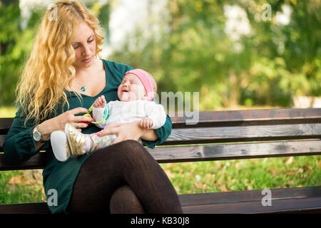 Maman apaise un bébé qui pleure, assis sur un banc de parc Banque D'Images