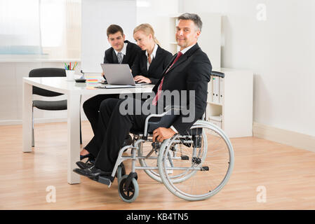 Mature businessman sur fauteuil roulant avec des collègues de bureau Banque D'Images