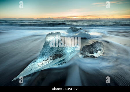 Morceaux de glace de glacier échoués sur une plage de sable volcanique noir, au lever du soleil près de jokulsarlon glacial lagoon, le sud de l'islande Banque D'Images