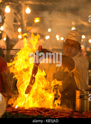 L'homme local cooking sausages sur feu ouvert à l'un des stands de nourriture dans la place Djemaa el Fna, Marrakech, Maroc, afrique du nord Banque D'Images