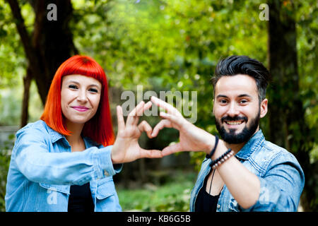 Couple d'amoureux formant un cœur avec leurs mains dans un parc Banque D'Images