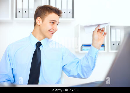 Portrait of young businessman lancer un avion en papier sur son lieu de travail à bright office Banque D'Images