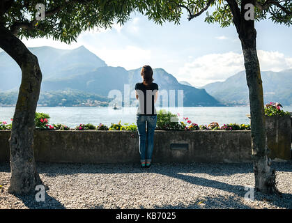 Vue arrière de young woman relaxing on quai pittoresque de montagne lac de Côme en Italie. locations de contexte Banque D'Images