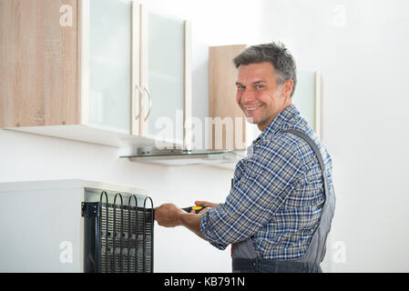 Portrait of happy young handyman réparation réfrigérateur à la maison Banque D'Images