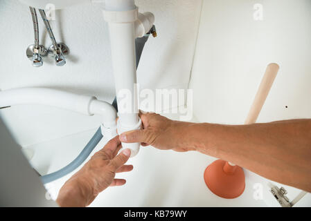 Image recadrée de plombier travaillant sur les tuyaux sous l'évier de cuisine Banque D'Images