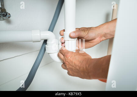Image recadrée de plombier travaillant sur les tuyaux sous l'évier de cuisine Banque D'Images
