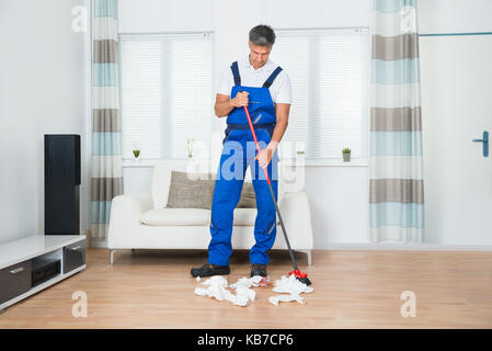 Toute la longueur de balayage janitor mâle sur marbre dans les papiers froissés de séjour Banque D'Images