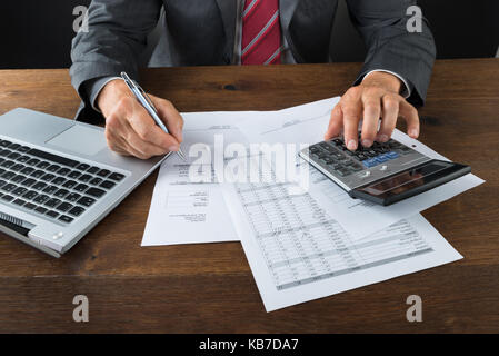 Portrait of businessman vérification avec la calculatrice et l'ordinateur portable à 24 Banque D'Images