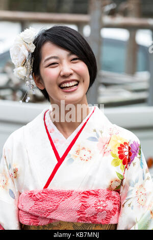 Le Japon. Tête et des épaules de la jeune femme japonaise riant en kimono de couleur crème. Fleurs blanches dans les cheveux. Face à Banque D'Images