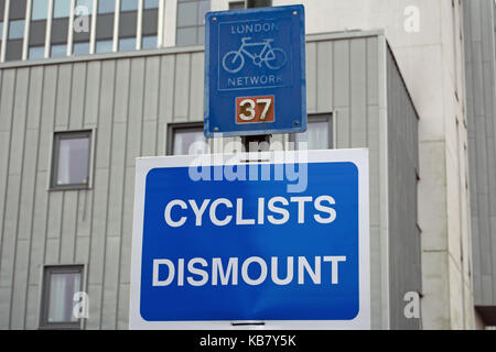 Les cyclistes démonter signer ci-dessous un london cycle réseau inscription, à Twickenham, Middlesex, Angleterre Banque D'Images