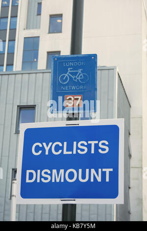 Les cyclistes démonter signer ci-dessous un london cycle réseau inscription, à Twickenham, Middlesex, Angleterre Banque D'Images