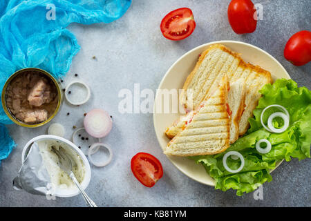 Sandwich double avec le thon et le fromage féta servi avec des feuilles de laitue sur une planche à découper en bois. Banque D'Images