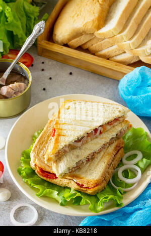 Sandwich double avec le thon et le fromage féta servi avec des feuilles de laitue sur une planche à découper en bois. Banque D'Images