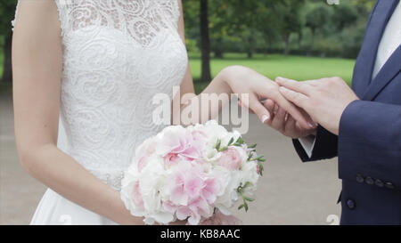 Les jeunes mariés à l'extérieur. Les mariés marcher ensemble dans le parc en hiver ou en été et se tenant la main. happy young couple walking in park parmi les buissons de cerise. Banque D'Images