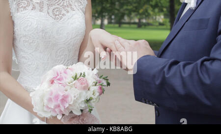 Les jeunes mariés à l'extérieur. Les mariés marcher ensemble dans le parc en hiver ou en été et se tenant la main. happy young couple walking in park parmi les buissons de cerise. Banque D'Images