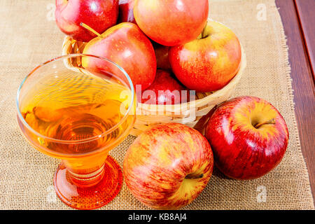 Verre de cidre et pommes rouges dans le rustique panier en osier sur fond de bois Banque D'Images