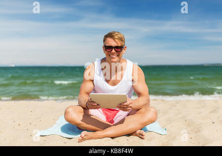 Happy smiling young man with tablet pc sur beach Banque D'Images