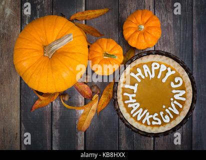 Tarte à la citrouille avec happy thanksgiving. texte affiché avec des citrouilles, des feuilles d'automne doré, et glands sur table rustique. vue d'en haut. Banque D'Images