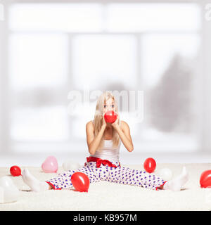 Jeune femme blonde assise sur son ensemble blanc-tapis de sol et du gonflage ballon rouge près de window Banque D'Images