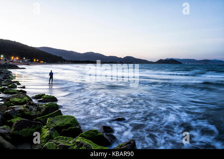 Silhouette d'un homme qui pêche à la plage d'Armacao au crépuscule. Florianopolis, Santa Catarina, Brésil. Banque D'Images