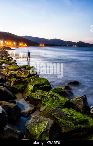 Silhouette d'un homme qui pêche à la plage d'Armacao au crépuscule. Florianopolis, Santa Catarina, Brésil. Banque D'Images