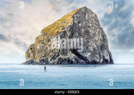 Un aventurier sur un stand up paddle board fait un voyage en solitaire vers haystack rock off of cape kiwanda, Pacific city, Oregon, united states Banque D'Images