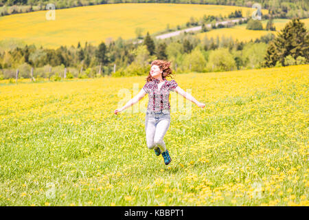 Dos de jeune femme courir, sauter dans l'air et souriant sur les champs de fleurs de pissenlit jaune campagne en été l'herbe dans l'île d'Orléans, Québec, Canada Banque D'Images