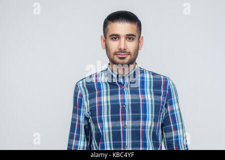 Homme barbu élégant avec un appel des yeux sombres en souriant. caméra businessman with beard souriant ayant regarder positif. piscine, studio shot dos gris. Banque D'Images