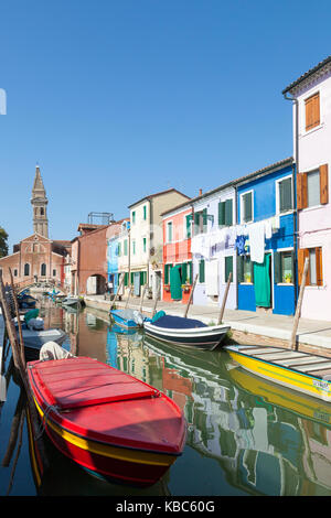 Burano, Venise, Vénétie, Italie du clocher de l'église San Martino avec des maisons et des bateaux sur un canal tranquille Banque D'Images