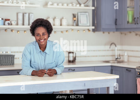 Souriante jeune femme africaine appuyée sur son île de cuisine Banque D'Images