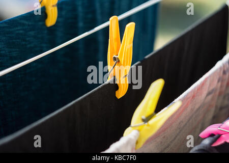 Close-up of clothespin holding en plastique jaune t-shirt noir sur le fil Banque D'Images