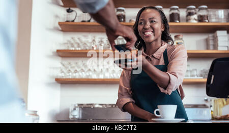Smiling barista en utilisant la technologie NFC pour le paiement d'un client Banque D'Images