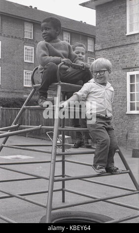 70, tableau historique des trois jeunes garçons jouer ensemble sur une escalade dans une pépinière aire de jeux sur un ensemble immobilier conseil à Deptford, le sud de Londres, Angleterre, Royaume-Uni. Banque D'Images