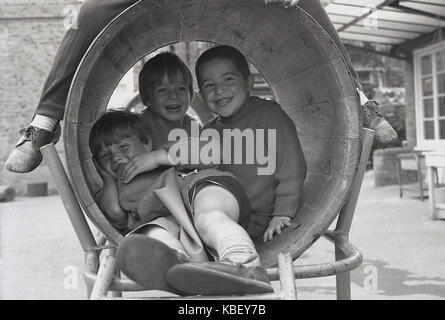 Années 1970, historiques, les enfants ont beaucoup de plaisir à jouer ensemble dans un tonneau tunnel dans un jeu pour enfants sur un conseil estat à Deptford, Londres, Angleterre, Royaume-Uni. Banque D'Images