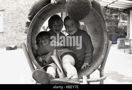 Années 1970, historiques, les enfants ont beaucoup de plaisir à jouer ensemble sur un baril tunnel dans un jeu pour enfants sur un conseil estat à Deptford, Londres, Angleterre, Royaume-Uni. Banque D'Images