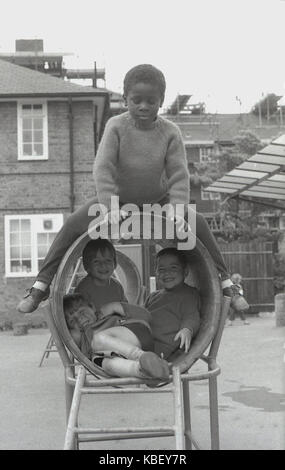 Années 1970, historiques, les enfants ont beaucoup de plaisir à jouer ensemble dans un tonneau tunnel dans un jeu pour enfants sur un conseil estat à Deptford, Londres, Angleterre, Royaume-Uni. Un garçon est assis sur le haut du canon, tandis que les autres "cacher" à l'intérieur. Banque D'Images