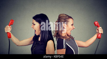 Communication concept. Deux femmes en colère crier par d'autres au téléphone isolé sur fond gris. Banque D'Images