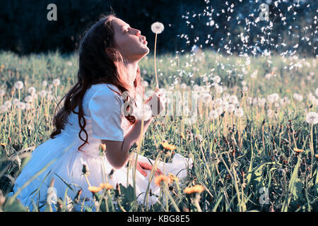 Teen girl blowing seeds à partir d'une fleur de pissenlit spring park Banque D'Images