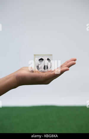 Close-up of hand holding football acrylique cube contre fond blanc Banque D'Images