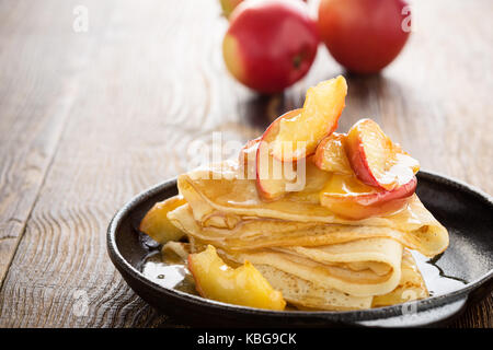 Crêpes maison servi avec des pommes caramélisées et sauce au caramel dans la poêle en fonte sur la table en bois en milieu rural Banque D'Images